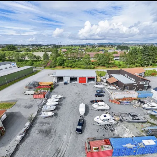 Anlegget på Avaldsnes sett fra luften: hallen med røde porter, båter på land rundt og containere langs plassen