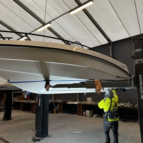 Båt løftet på lift mens en montør i refleksvest arbeider under skroget